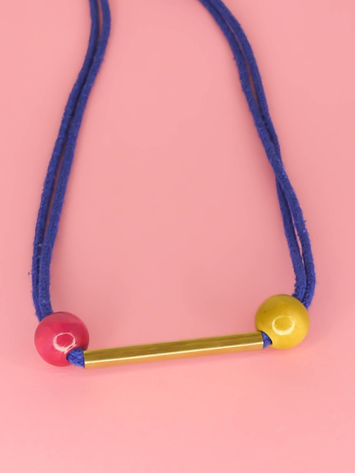 Cobalt blue rope bar necklace with a brass bar with contrasting wooden beads in pink and green with a brass clasp closure