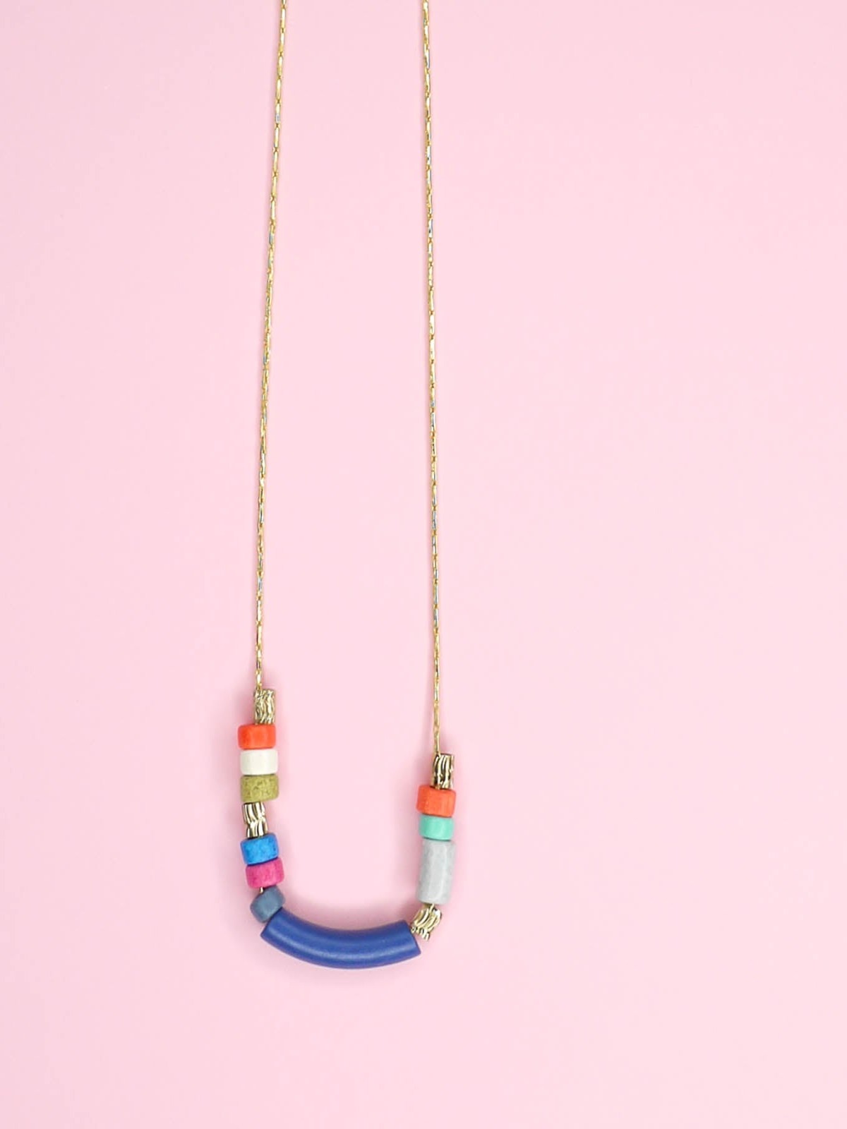 Delicate ceramic bead necklace with a blue curved bar bead, multicoloured ceramic tube beads and brass tube beads strung on a gold plated snake chain