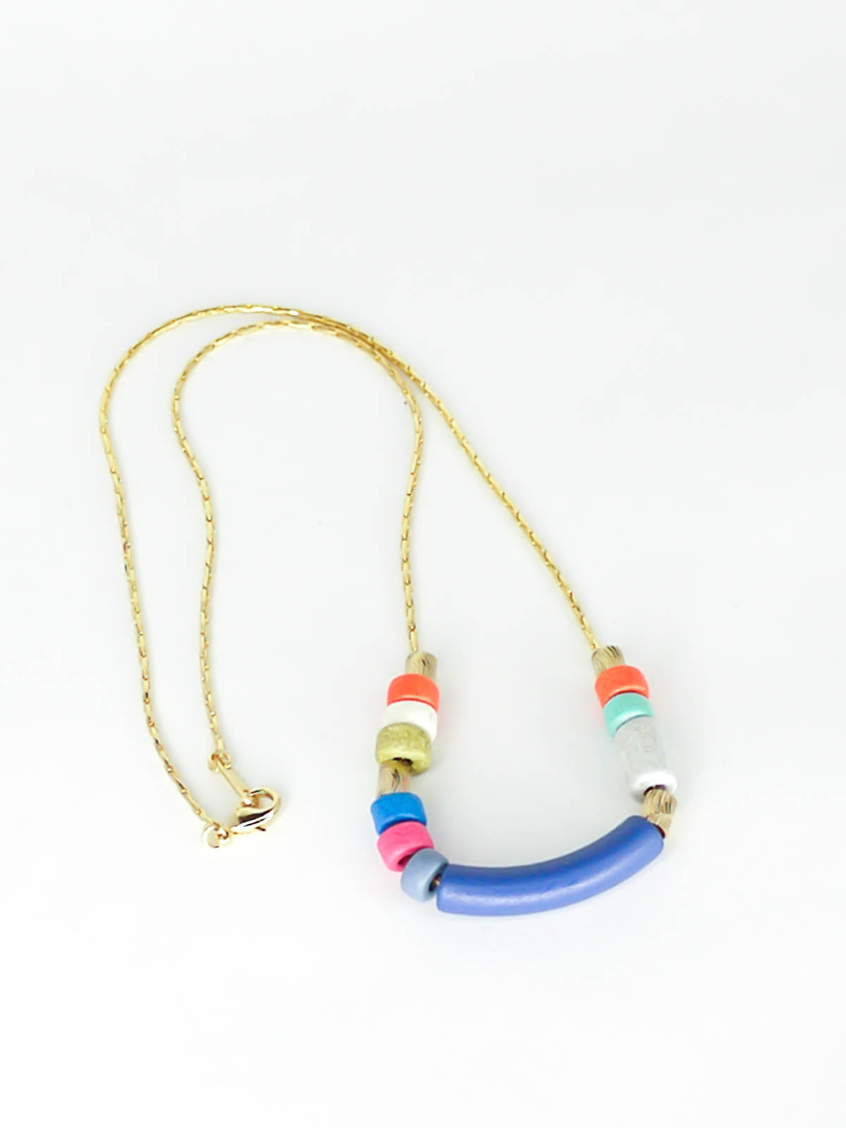 Delicate ceramic bead necklace with a blue curved bar bead, multicoloured ceramic tube beads and brass tube beads strung on a gold plated snake chain