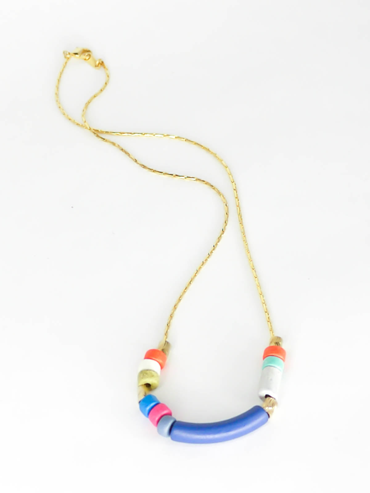 Delicate ceramic bead necklace with a blue curved bar bead, multicoloured ceramic tube beads and brass tube beads strung on a gold plated snake chain