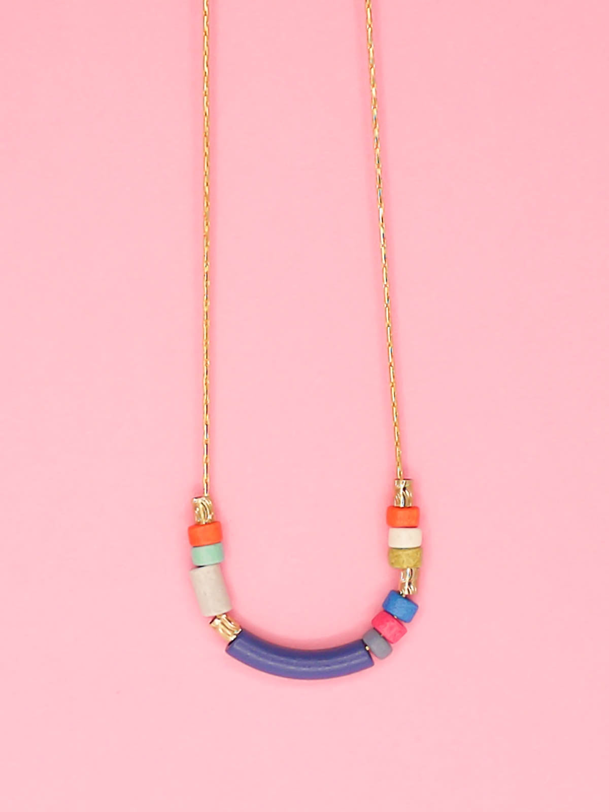 Delicate ceramic bead necklace with a blue curved bar bead, multicoloured ceramic tube beads and brass tube beads strung on a gold plated snake chain