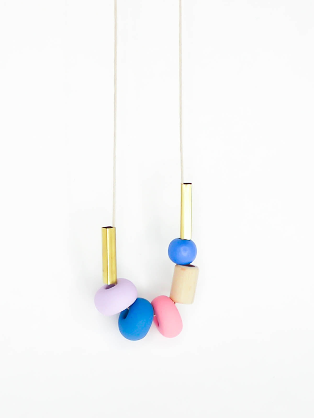 Lightweight geometric colourful bead necklace with 3 handmade polymer clay beads in lilac, blue & pink- wood tube bead & blue wood bead with brass tube beads on either side. Strung on a thin strong cotton cord with a blue wood bead knotted at the end