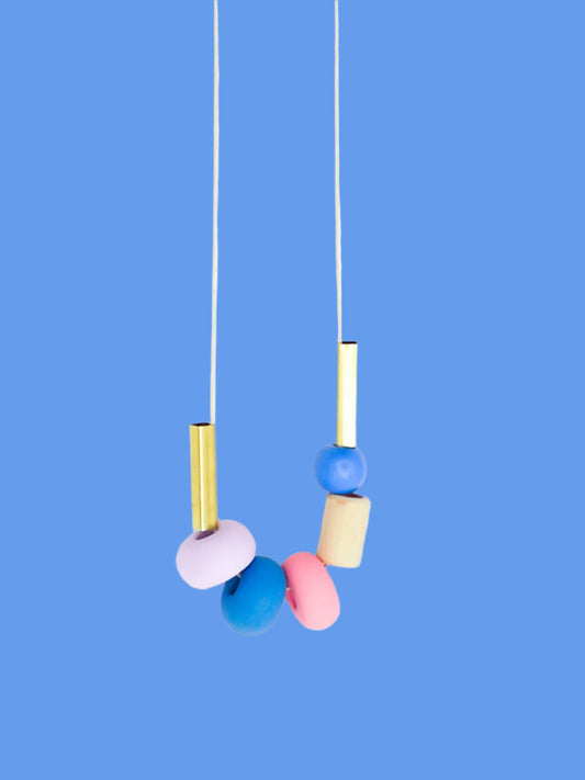 Lightweight geometric colourful bead necklace with 3 handmade polymer clay beads in lilac, blue & pink- wood tube bead & blue wood bead with brass tube beads on either side. Strung on a thin strong cotton cord with a blue wood bead knotted at the end