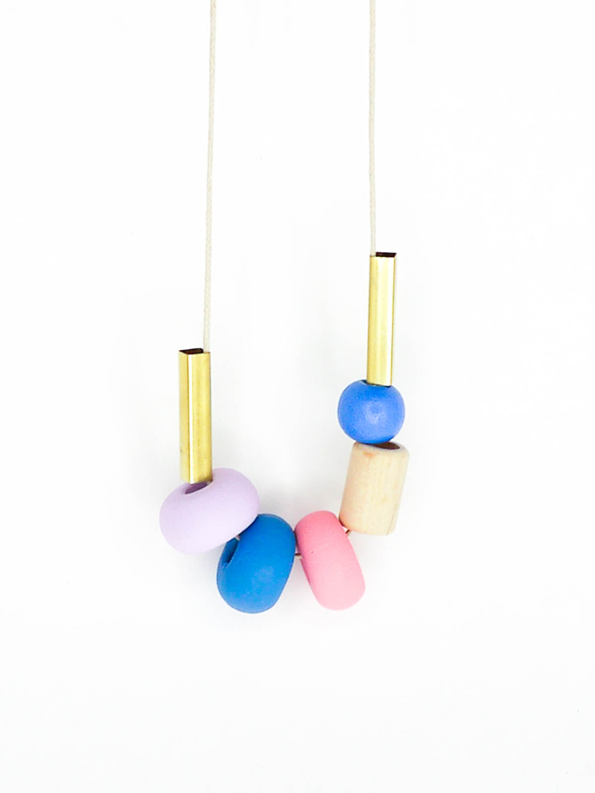 Lightweight geometric colourful bead necklace with 3 handmade polymer clay beads in lilac, blue & pink- wood tube bead & blue wood bead with brass tube beads on either side. Strung on a thin strong cotton cord with a blue wood bead knotted at the end