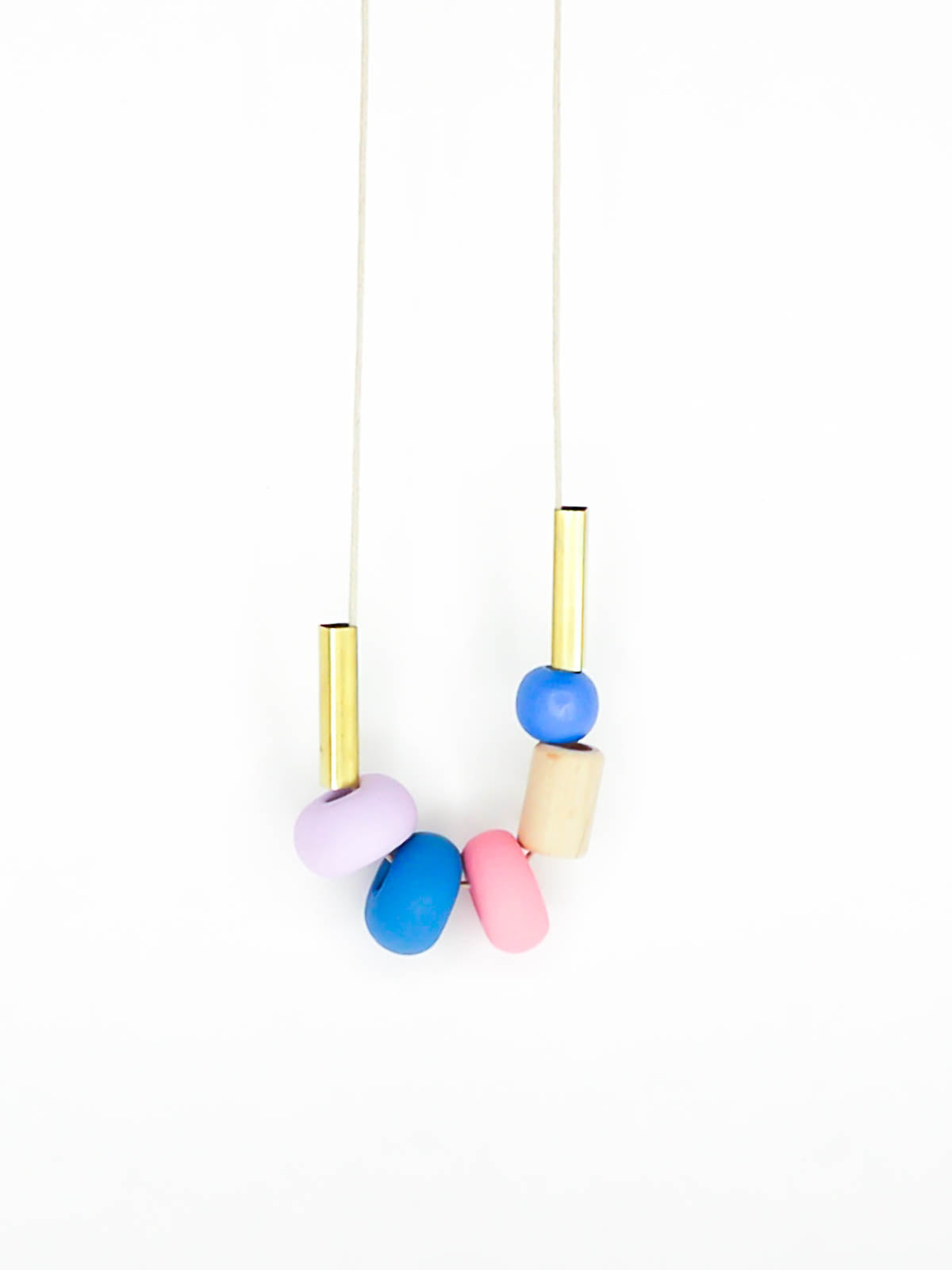 Lightweight geometric colourful bead necklace with 3 handmade polymer clay beads in lilac, blue & pink- wood tube bead & blue wood bead with brass tube beads on either side. Strung on a thin strong cotton cord with a blue wood bead knotted at the end