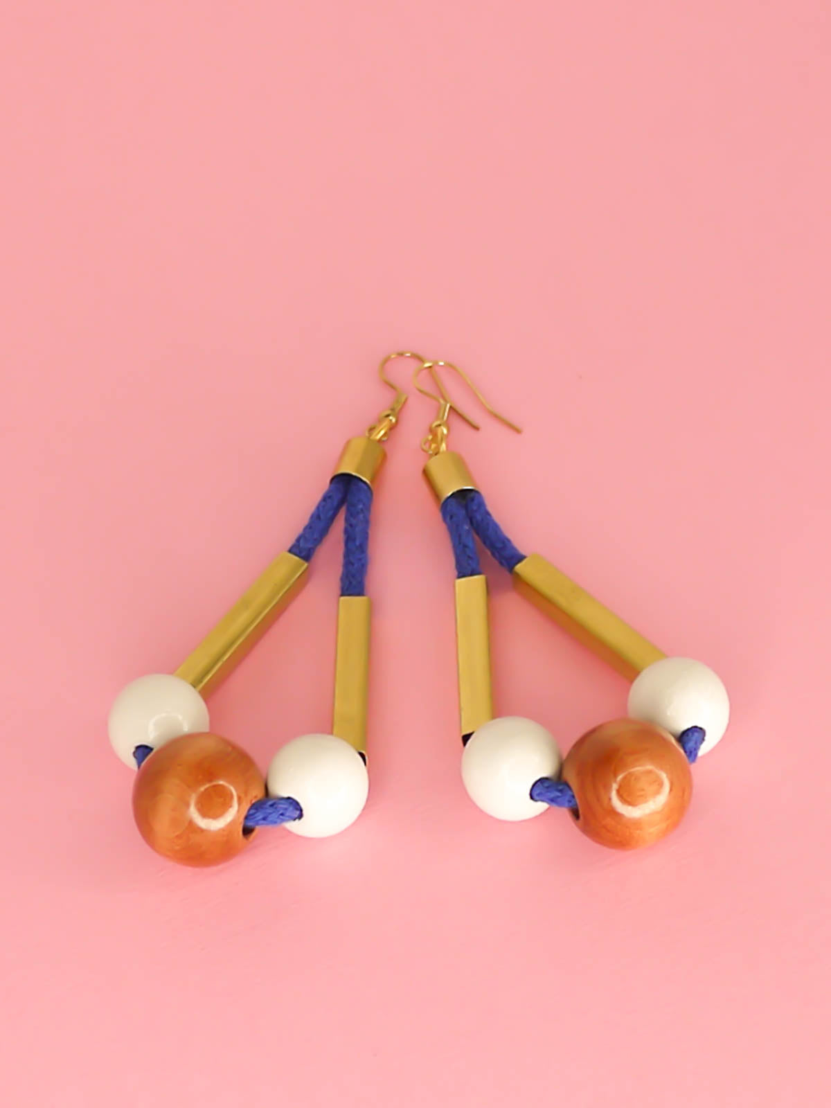 Long bead dangle statement earrings with wooden beads in white & brown & brass tube beads strung on cobalt blue cotton rope with brass end caps, hung from gold plated brass earring hooks.