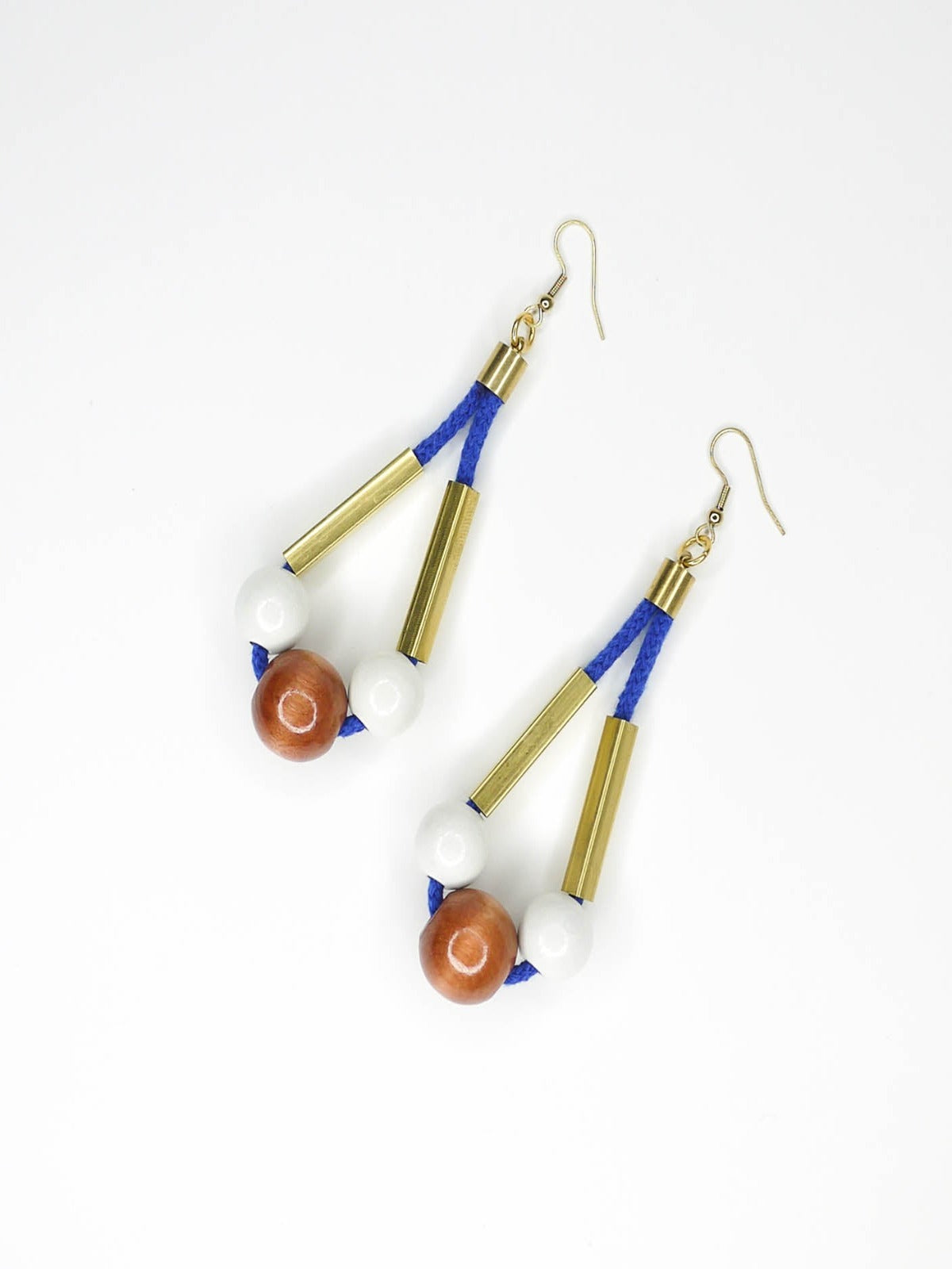 Long bead dangle statement earrings with wooden beads in white & brown & brass tube beads strung on cobalt blue cotton rope with brass end caps, hung from gold plated brass earring hooks.