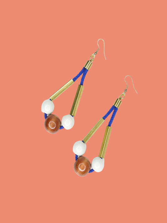 Long bead dangle statement earrings with wooden beads in white & brown & brass tube beads strung on cobalt blue cotton rope with brass end caps, hung from gold plated brass earring hooks.