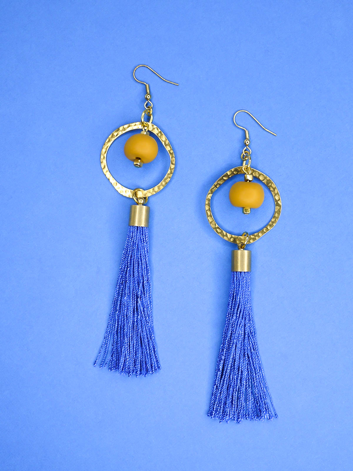 Long tassel statement earrings with gold plated ear wires, connected to a textured brass hoop with a mustard polymer clay bead dangling in the centre & a cobalt blue long tassel hung from the hoop