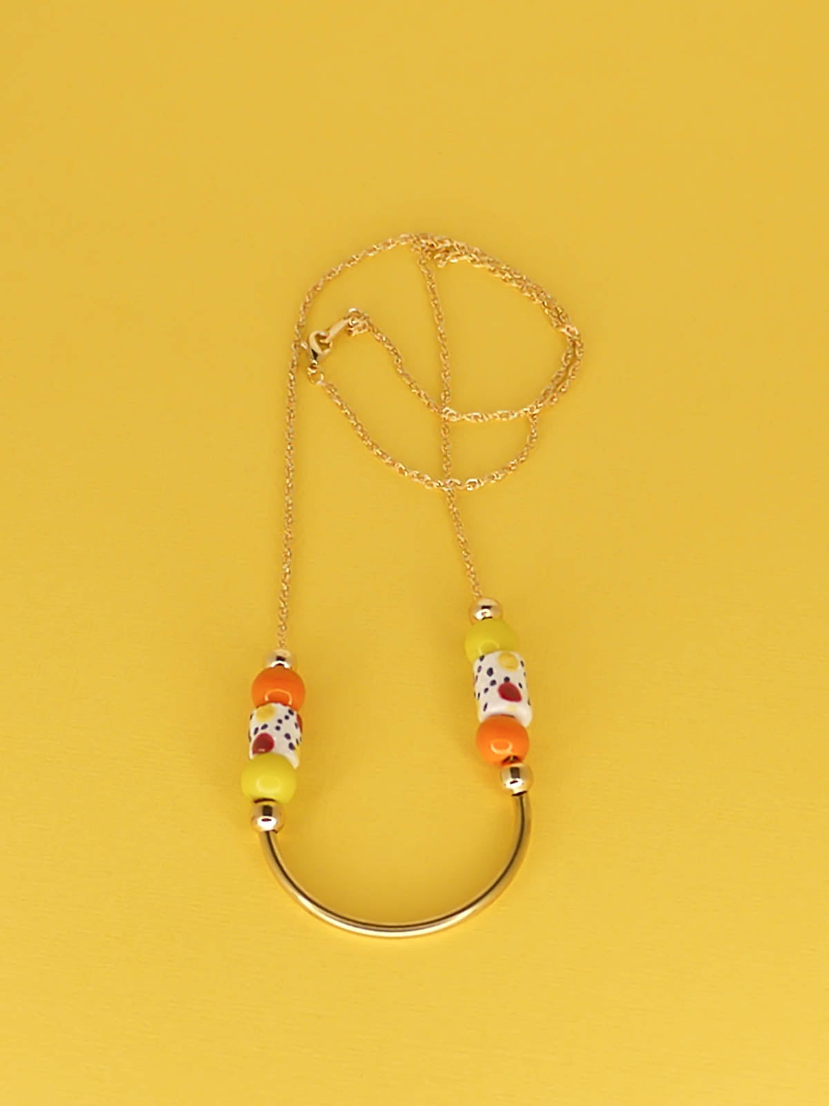 Lightweight beaded necklace with a brass curved bar in the centre and brass ball beads with orange & chartreuse ceramic ball beads and white spotted tube ceramic beads strung on both sides with a 24k gold plated snake chain