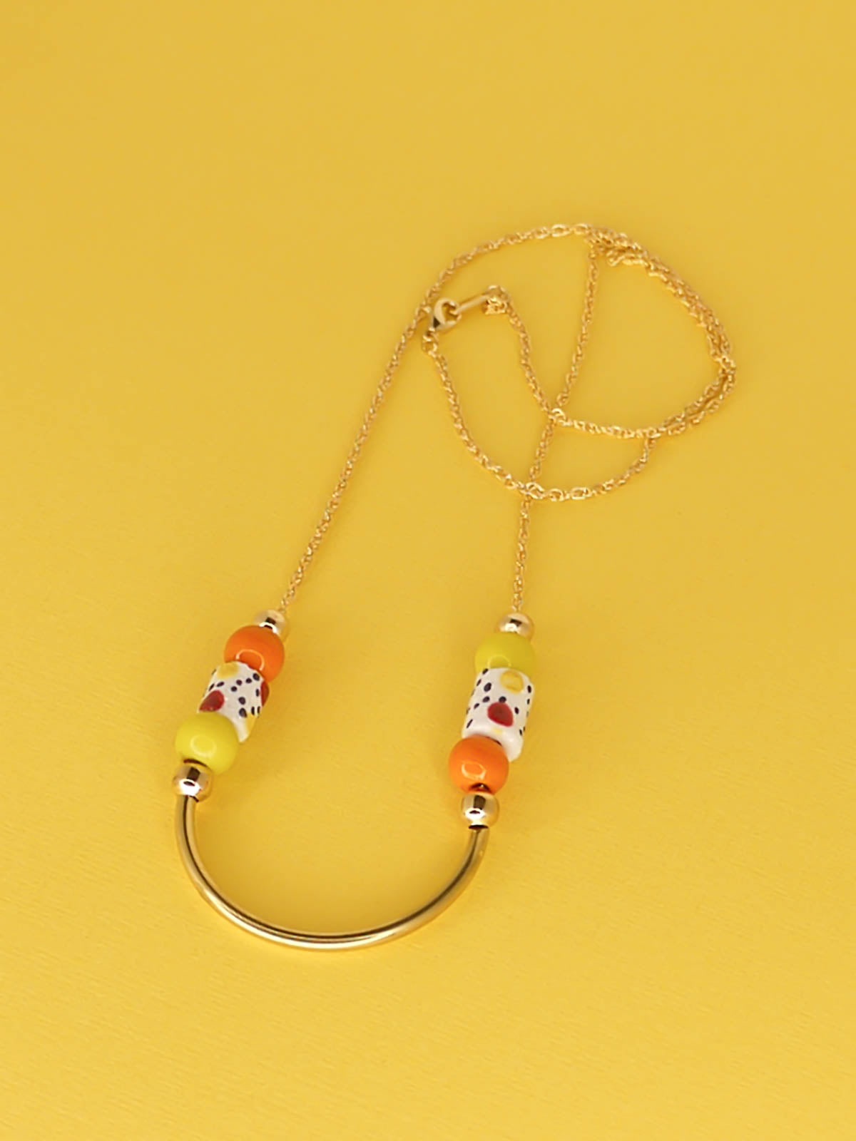 Lightweight beaded necklace with a brass curved bar in the centre and brass ball beads with orange & chartreuse ceramic ball beads and white spotted tube ceramic beads strung on both sides with a 24k gold plated snake chain