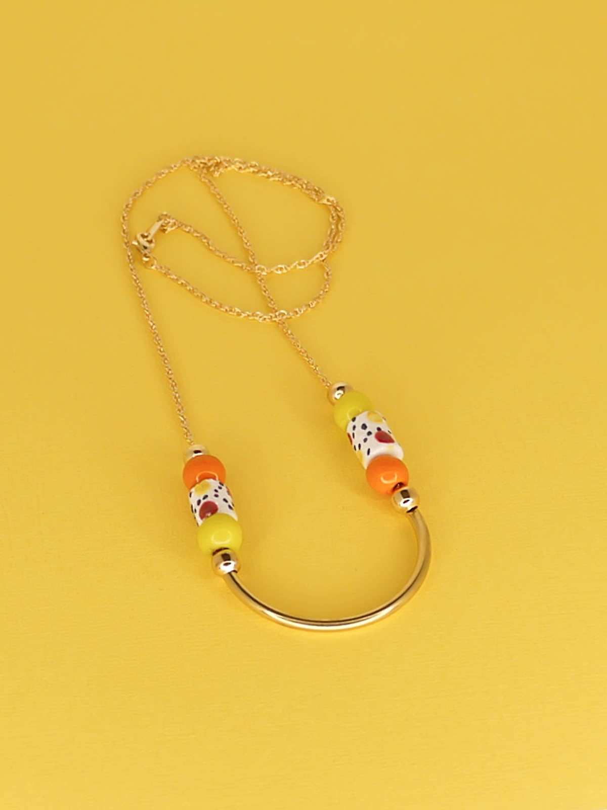 Lightweight beaded necklace with a brass curved bar in the centre and brass ball beads with orange & chartreuse ceramic ball beads and white spotted tube ceramic beads strung on both sides with a 24k gold plated snake chain