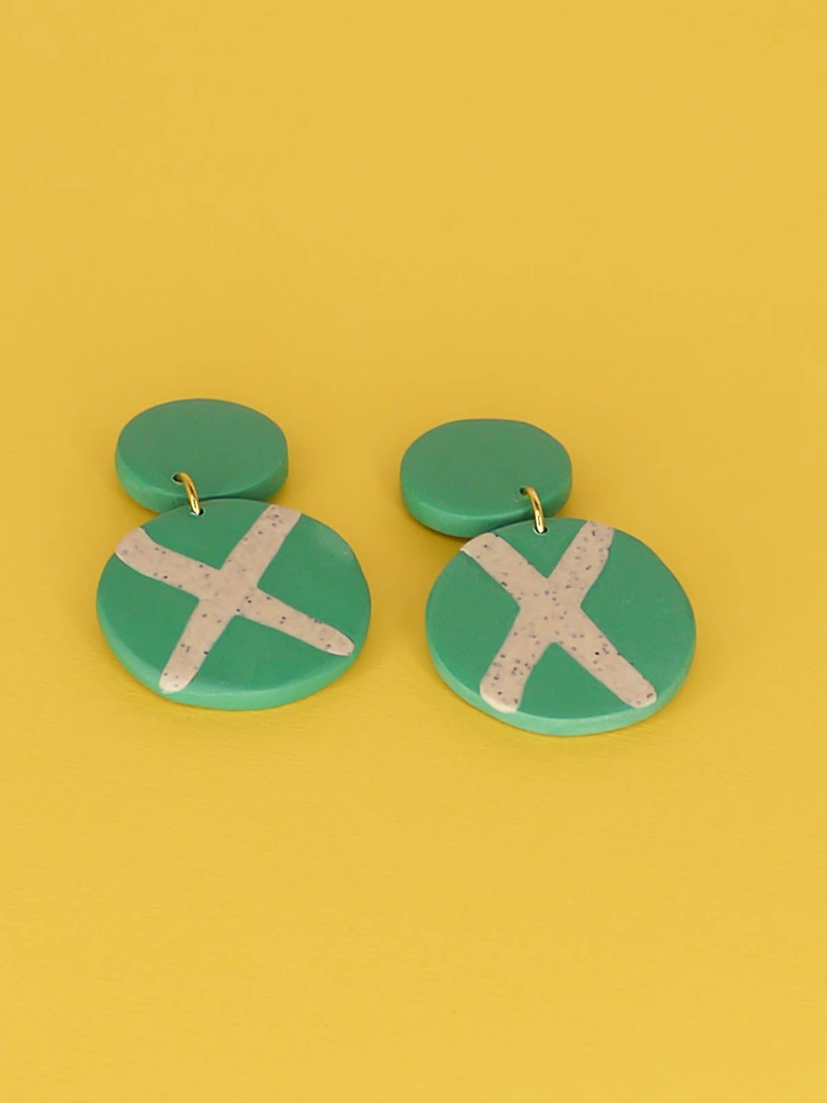 Polymer clay dangle statement earrings with a green stud connected to a green circle with a granite cross in the centre