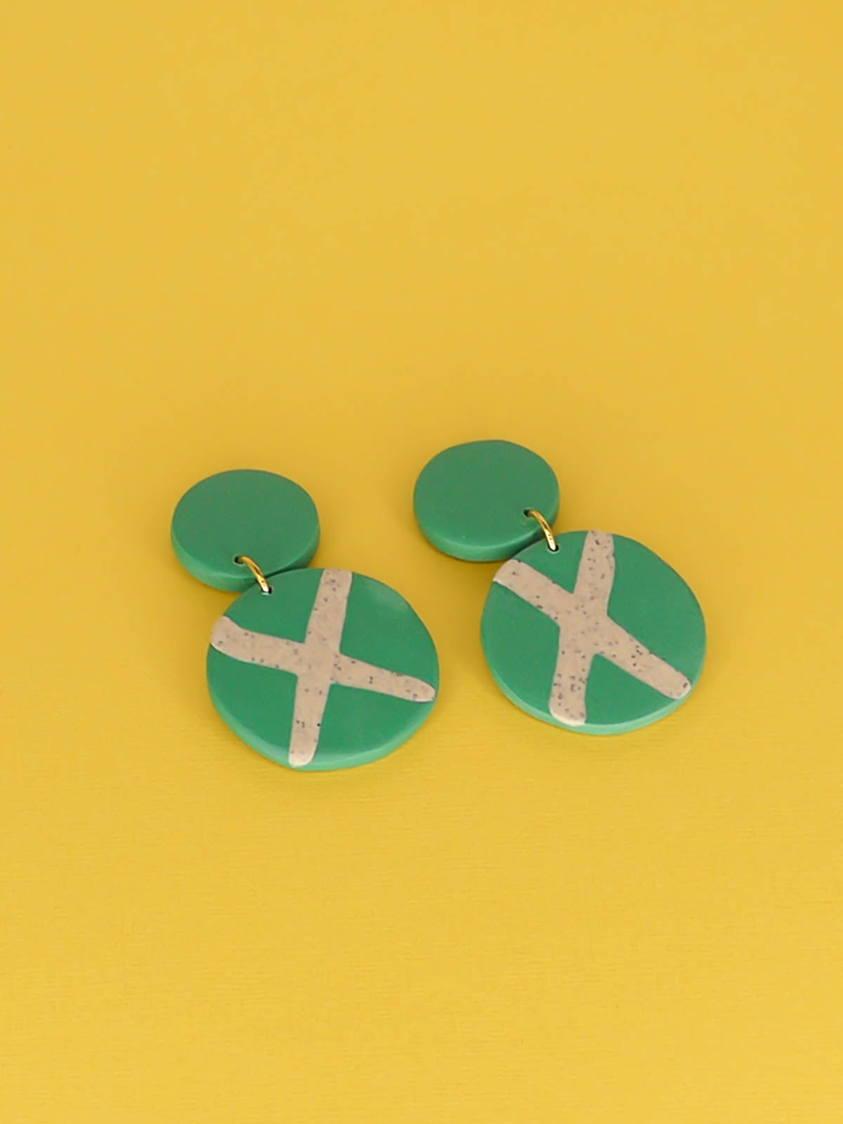 Polymer clay dangle statement earrings with a green stud connected to a green circle with a granite cross in the centre