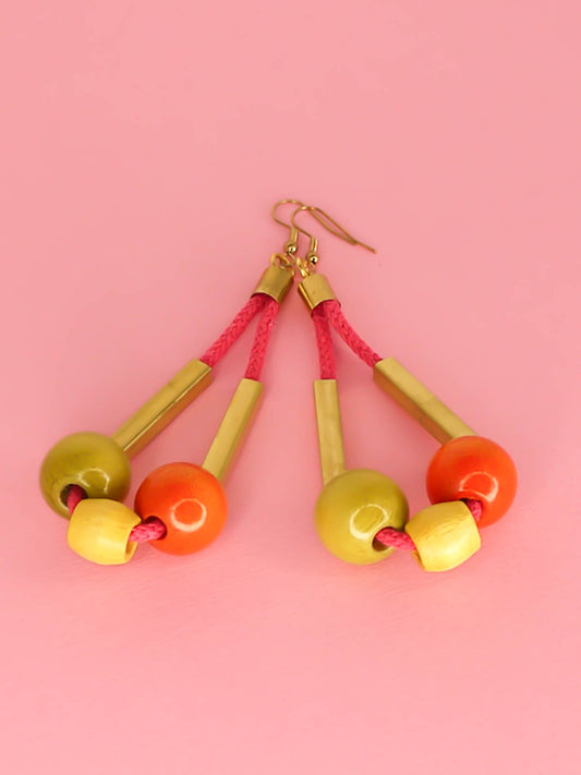 Long bead dangle statement earrings with wooden beads in green, orange & yellow & brass tube beads strung on hot pink cotton rope with brass end caps, hung from gold plated brass earring hooks.