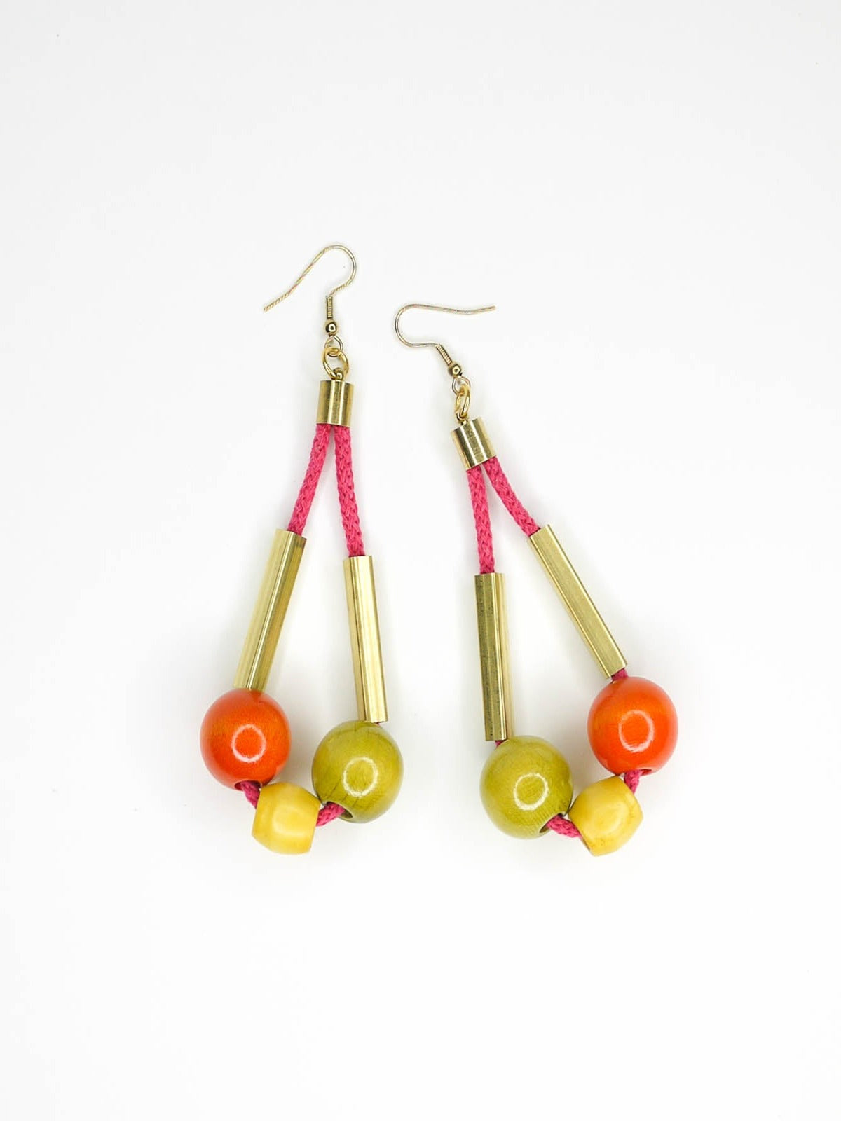 Long bead dangle statement earrings with wooden beads in green, orange & yellow & brass tube beads strung on hot pink cotton rope with brass end caps, hung from gold plated brass earring hooks.