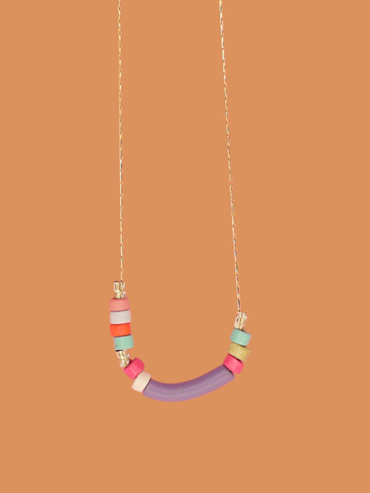 Dainty beaded ceramic necklace with a lilac curved bar bead, surrounded by textured brass tube beads and colourful ceramic beads in pink, turquoise, orange & white. Hung from a gold plated snake chain.