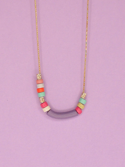 Dainty beaded ceramic necklace with a lilac curved bar bead, surrounded by textured brass tube beads and colourful ceramic beads in pink, turquoise, orange & white. Hung from a gold plated snake chain.