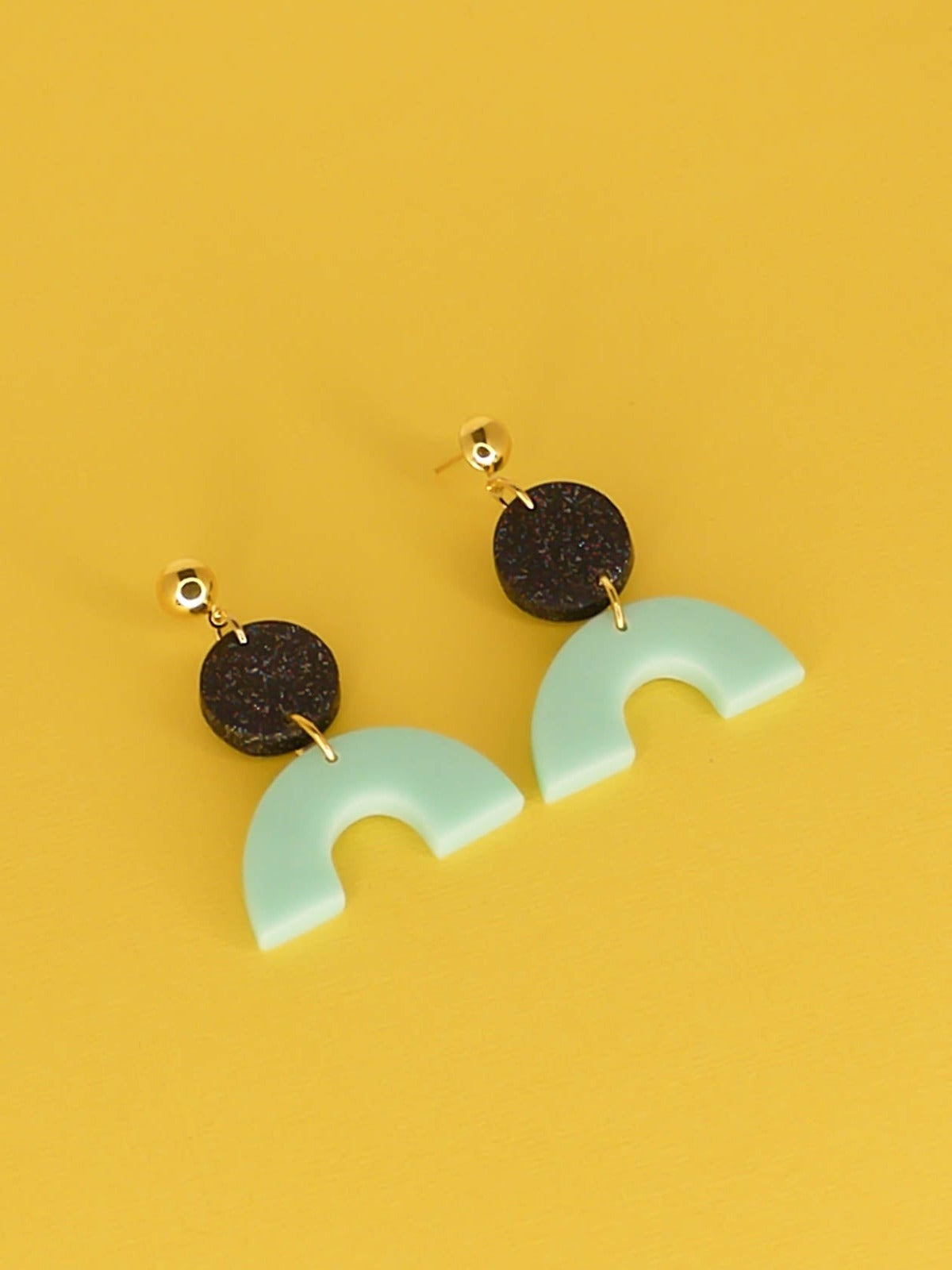 Geometric polymer clay dangle earrings earrings with a mint arch semi circle connected to a black glitter circle with gold plated brass circle studs.