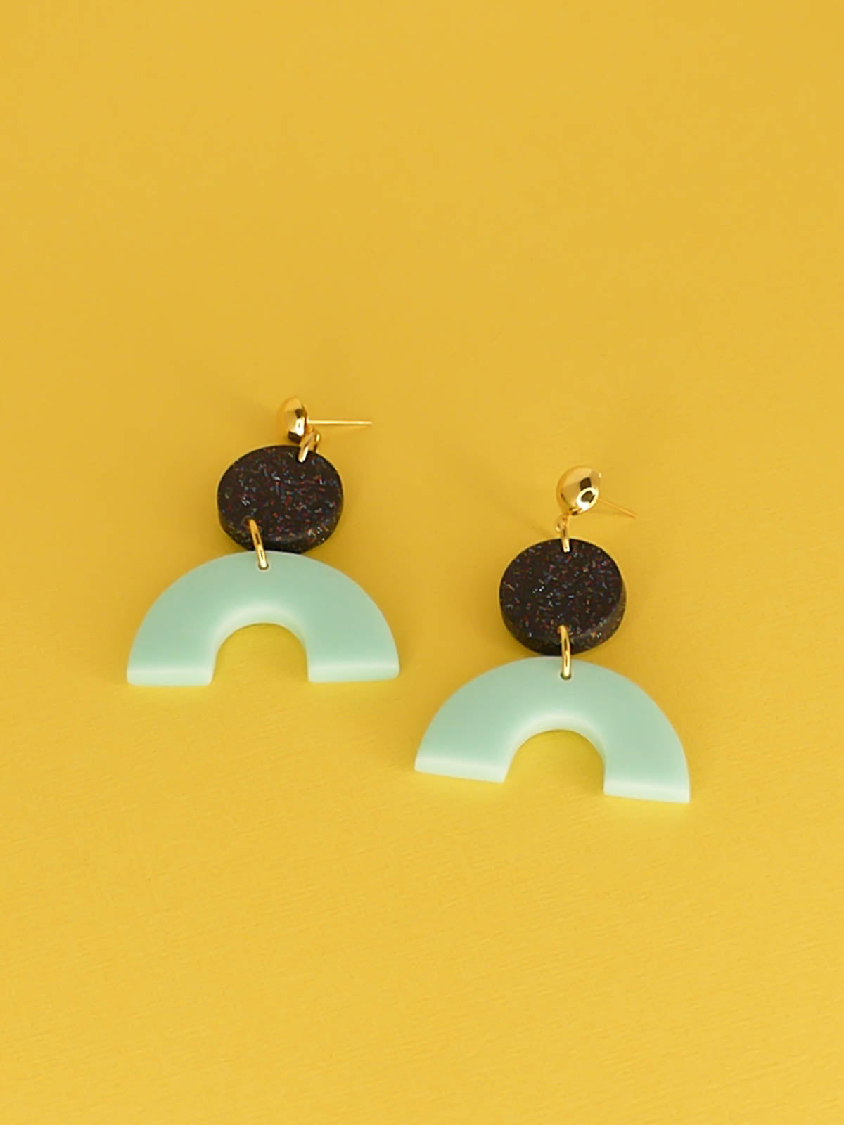 Geometric polymer clay dangle earrings earrings with a mint arch semi circle connected to a black glitter circle with gold plated brass circle studs.