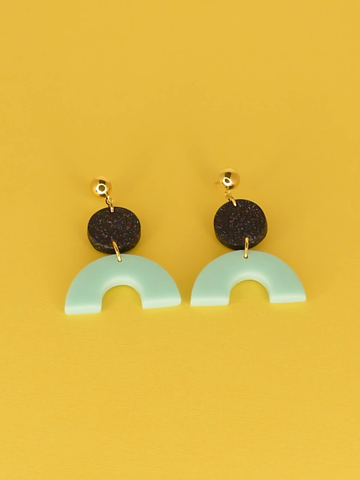 Geometric polymer clay dangle earrings earrings with a mint arch semi circle connected to a black glitter circle with gold plated brass circle studs.