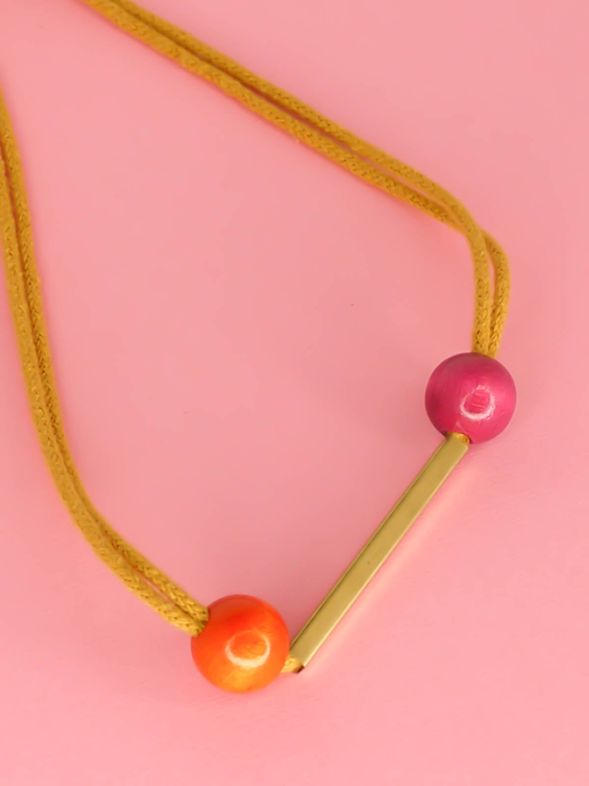 Mustard cotton rope bar necklace with a brass bar and contrasting wooden beads either side in orange and pink with a brass clasp