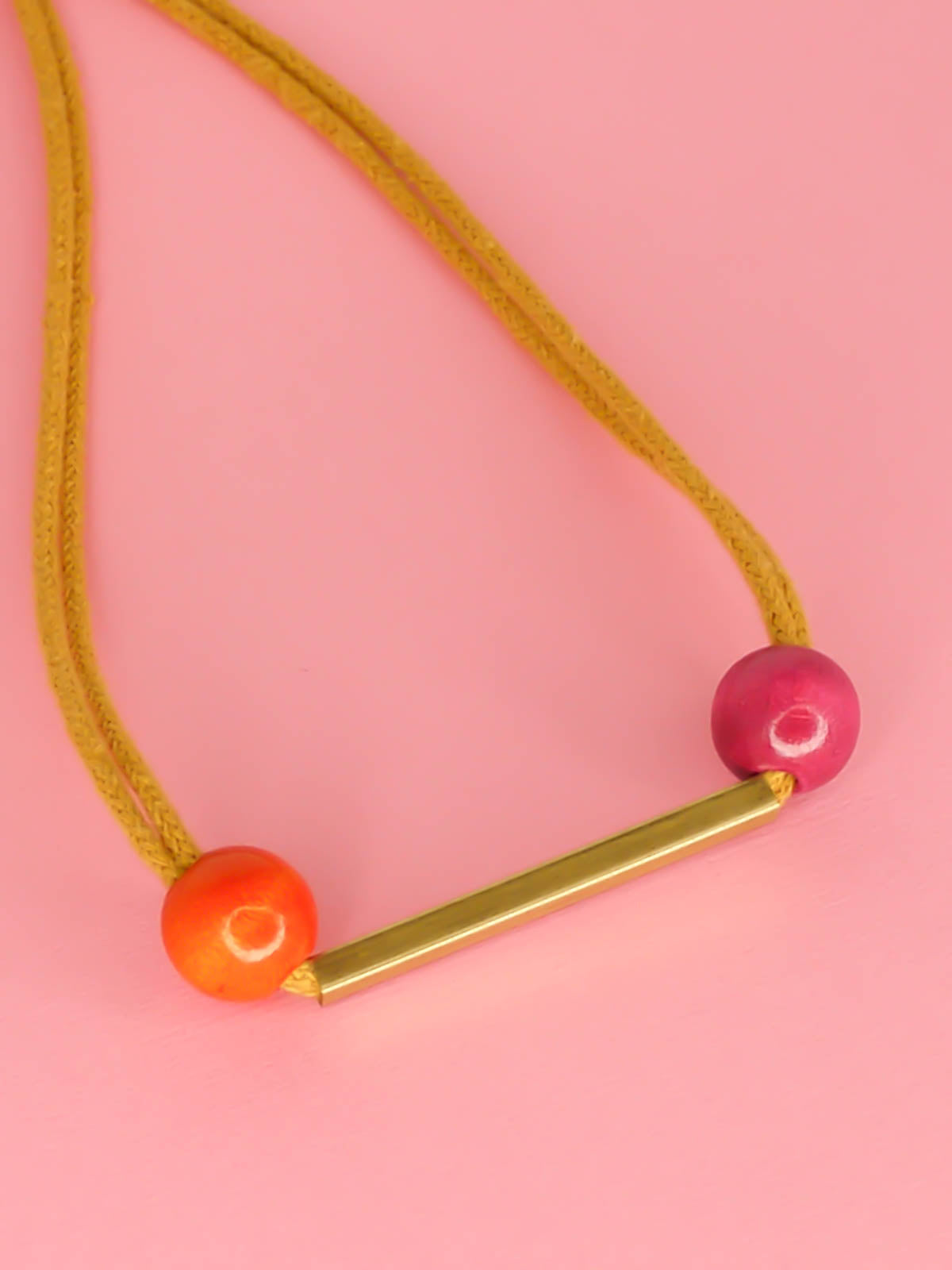 Mustard cotton rope bar necklace with a brass bar and contrasting wooden beads either side in orange and pink with a brass clasp