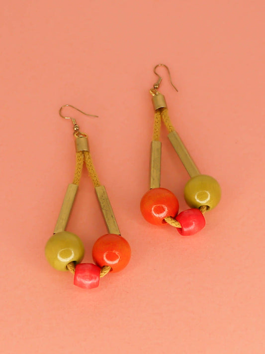 Long bead dangle statement earrings with wooden beads in watermelon, orange & green & brass tube beads strung on mustard coloured cotton rope with brass end caps, hung from gold plated brass earring hooks.