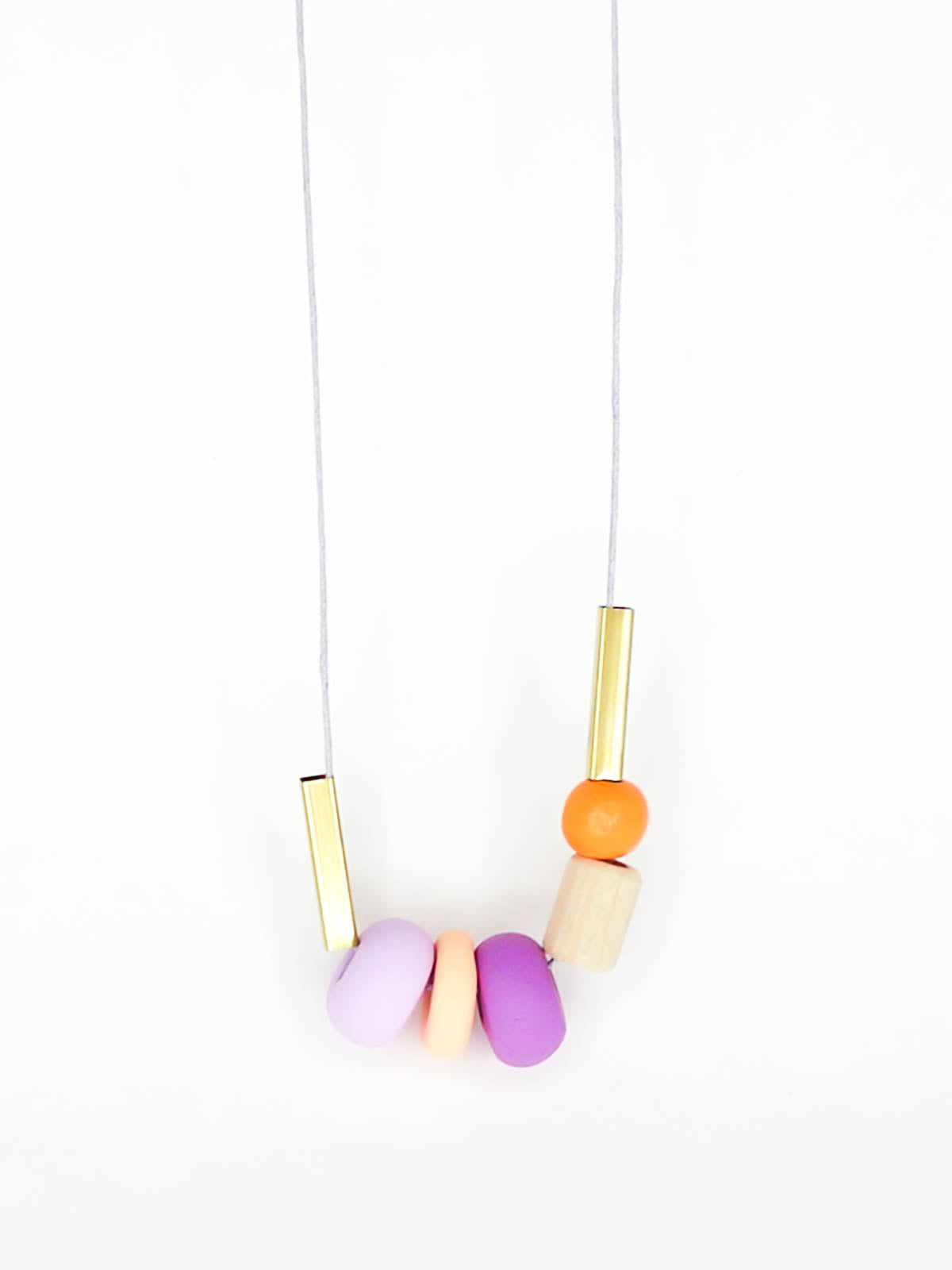 Lightweight geometric colourful bead necklace with 3 handmade polymer clay beads in peach, lilac & purple- wood tube bead & orange wood bead, brass tube beads on either side, strung on a cotton cord with a wood bead knotted at the end  