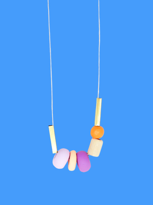 Lightweight geometric colourful bead necklace with 3 handmade polymer clay beads in peach, lilac & purple- wood tube bead & orange wood bead, brass tube beads on either side, strung on a cotton cord with a wood bead knotted at the end  
