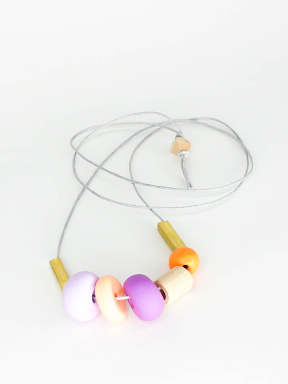 Lightweight geometric colourful bead necklace with 3 handmade polymer clay beads in peach, lilac & purple- wood tube bead & orange wood bead, brass tube beads on either side, strung on a cotton cord with a wood bead knotted at the end 