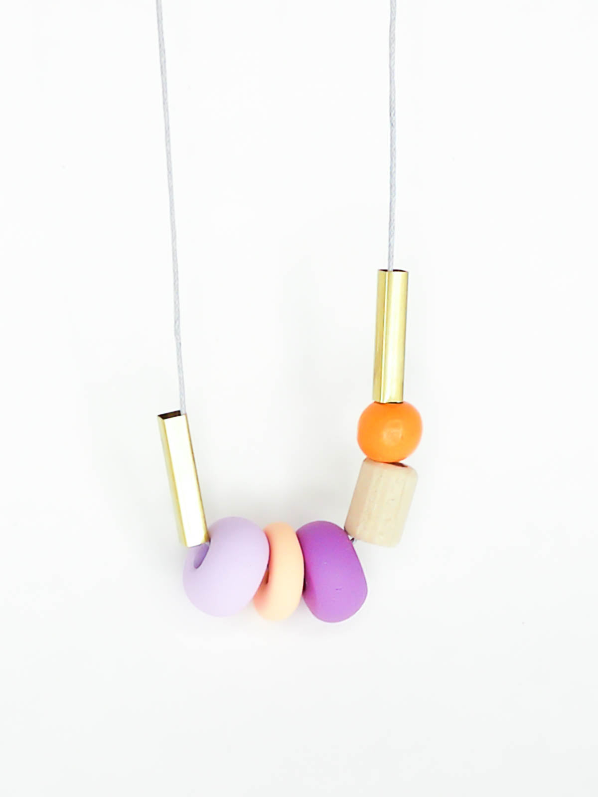 Lightweight geometric colourful bead necklace with 3 handmade polymer clay beads in peach, lilac & purple- wood tube bead & orange wood bead, brass tube beads on either side, strung on a cotton cord with a wood bead knotted at the end 