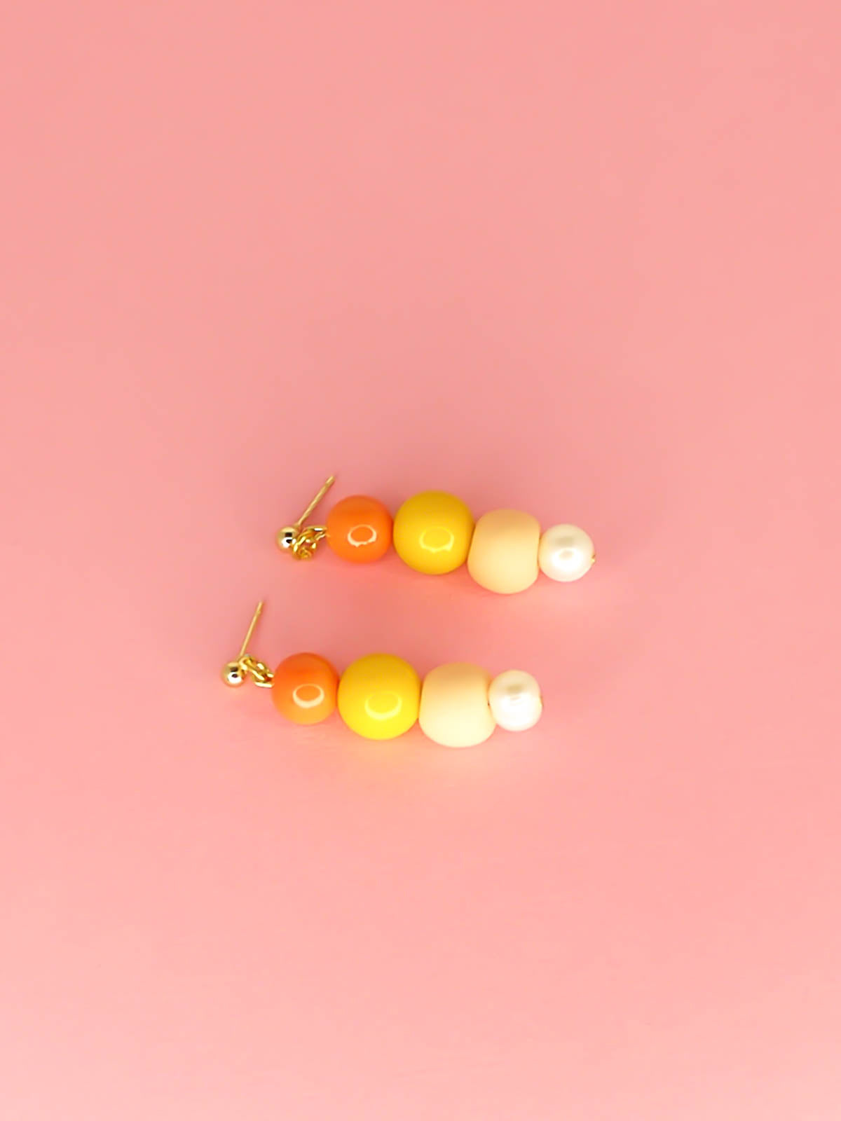 Pastel colour block earrings in orange & yellow glass beads, with a hand rolled polymer clay bead in peach and a mother of pearl bead, hung from 24k gold plated brass ball studs