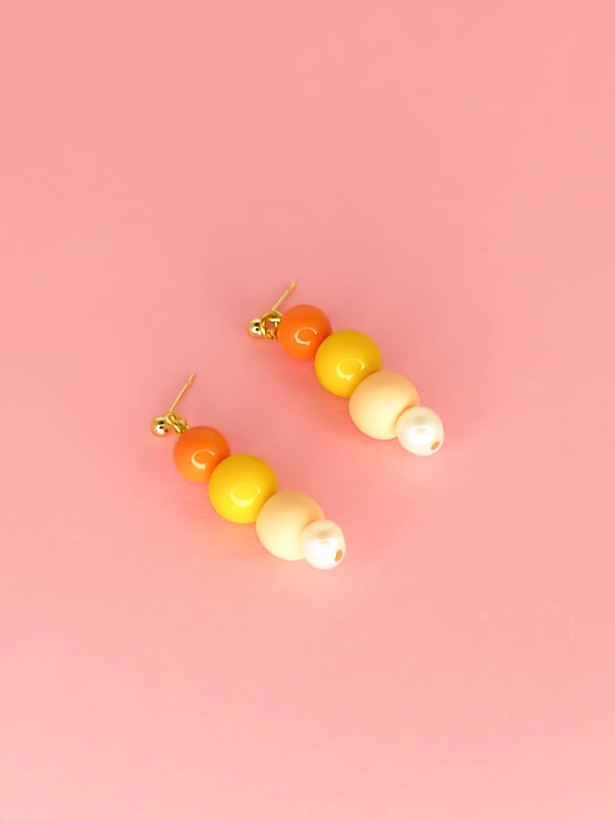 Pastel colour block earrings in orange & yellow glass beads, with a hand rolled polymer clay bead in peach and a mother of pearl bead, hung from 24k gold plated brass ball studs