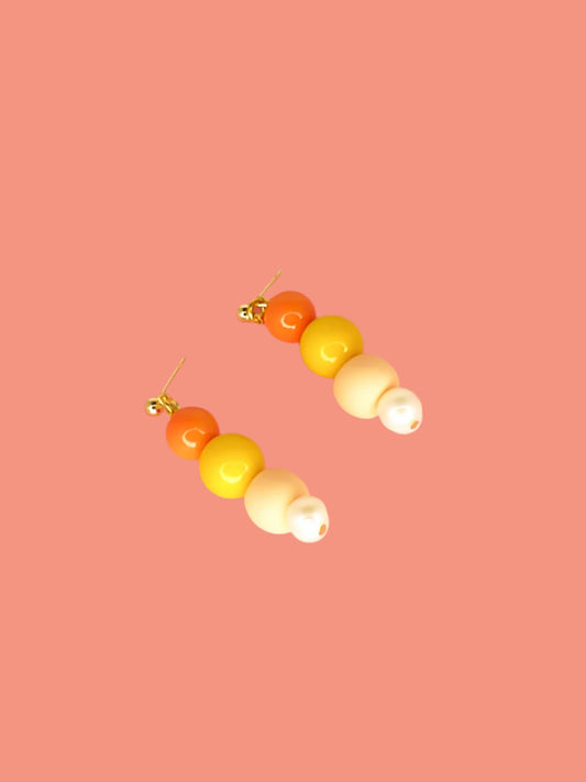 Pastel colour block earrings in orange & yellow glass beads, with a hand rolled polymer clay bead in peach and a mother of pearl bead, hung from 24k gold plated brass ball studs