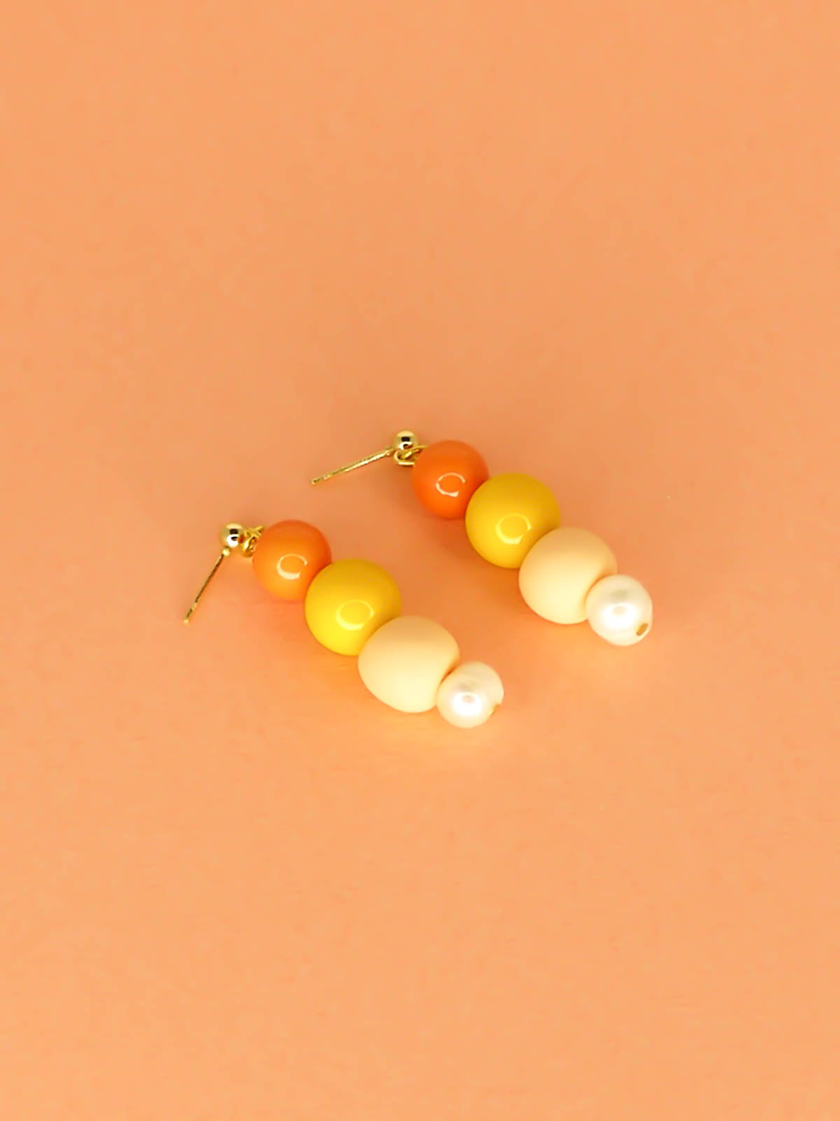 Pastel colour block earrings in orange & yellow glass beads, with a hand rolled polymer clay bead in peach and a mother of pearl bead, hung from 24k gold plated brass ball studs