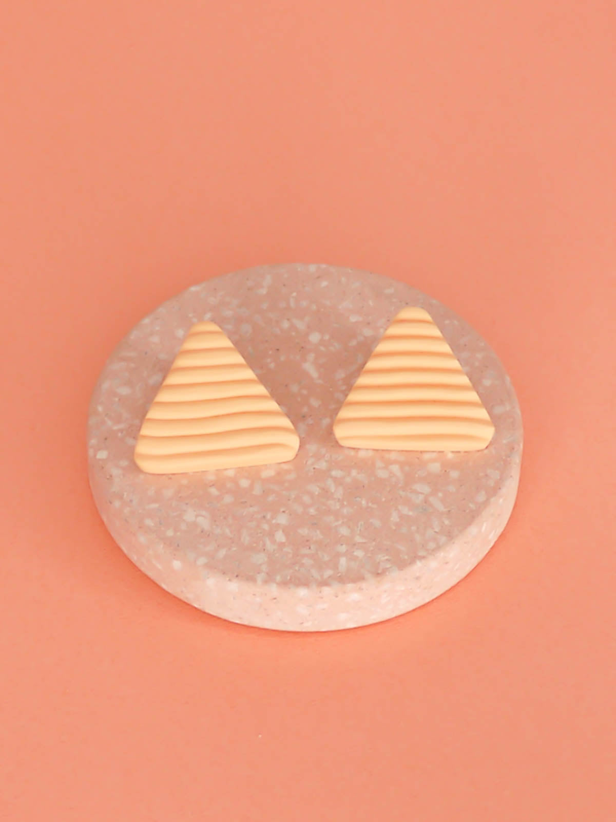 Lightweight peach polymer clay triangle stud earrings in a fluted striped texture with stainless steel studs.