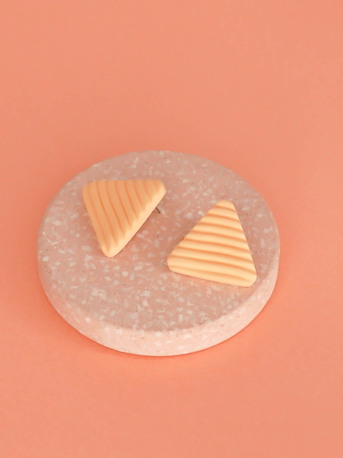 Lightweight peach polymer clay triangle stud earrings in a fluted striped texture with stainless steel studs.