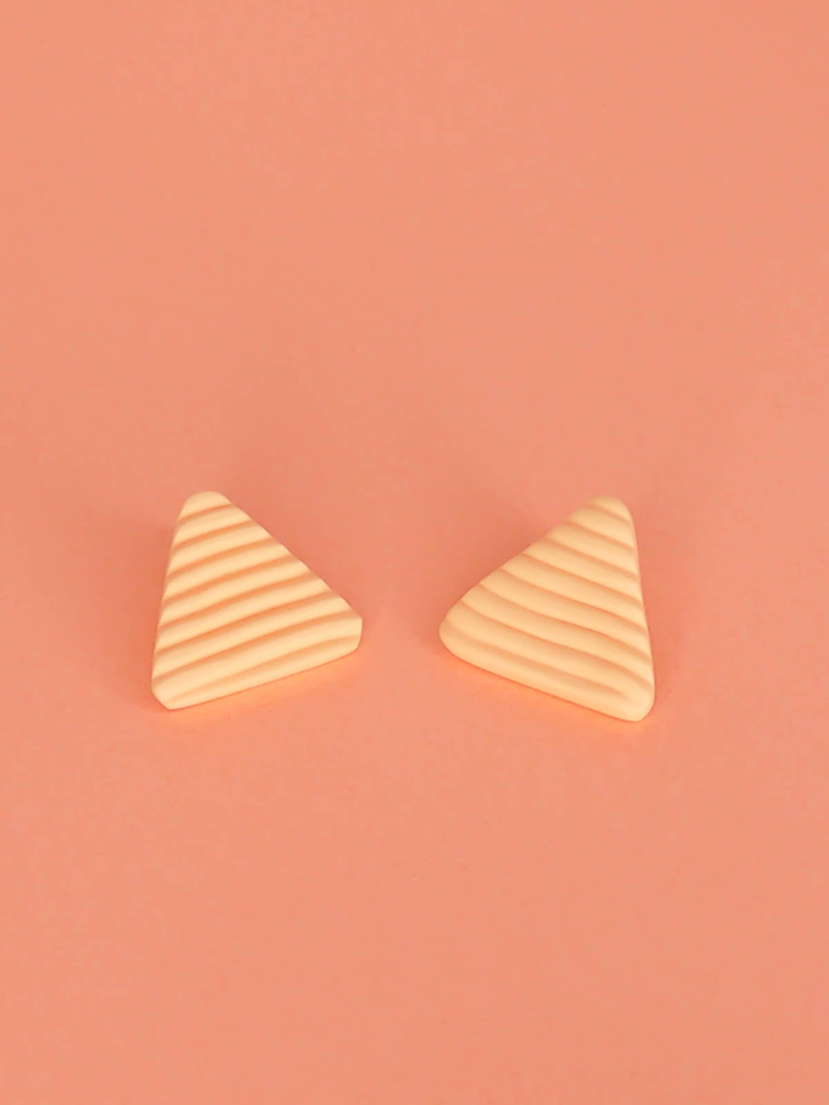 Lightweight peach polymer clay triangle stud earrings in a fluted striped texture with stainless steel studs.