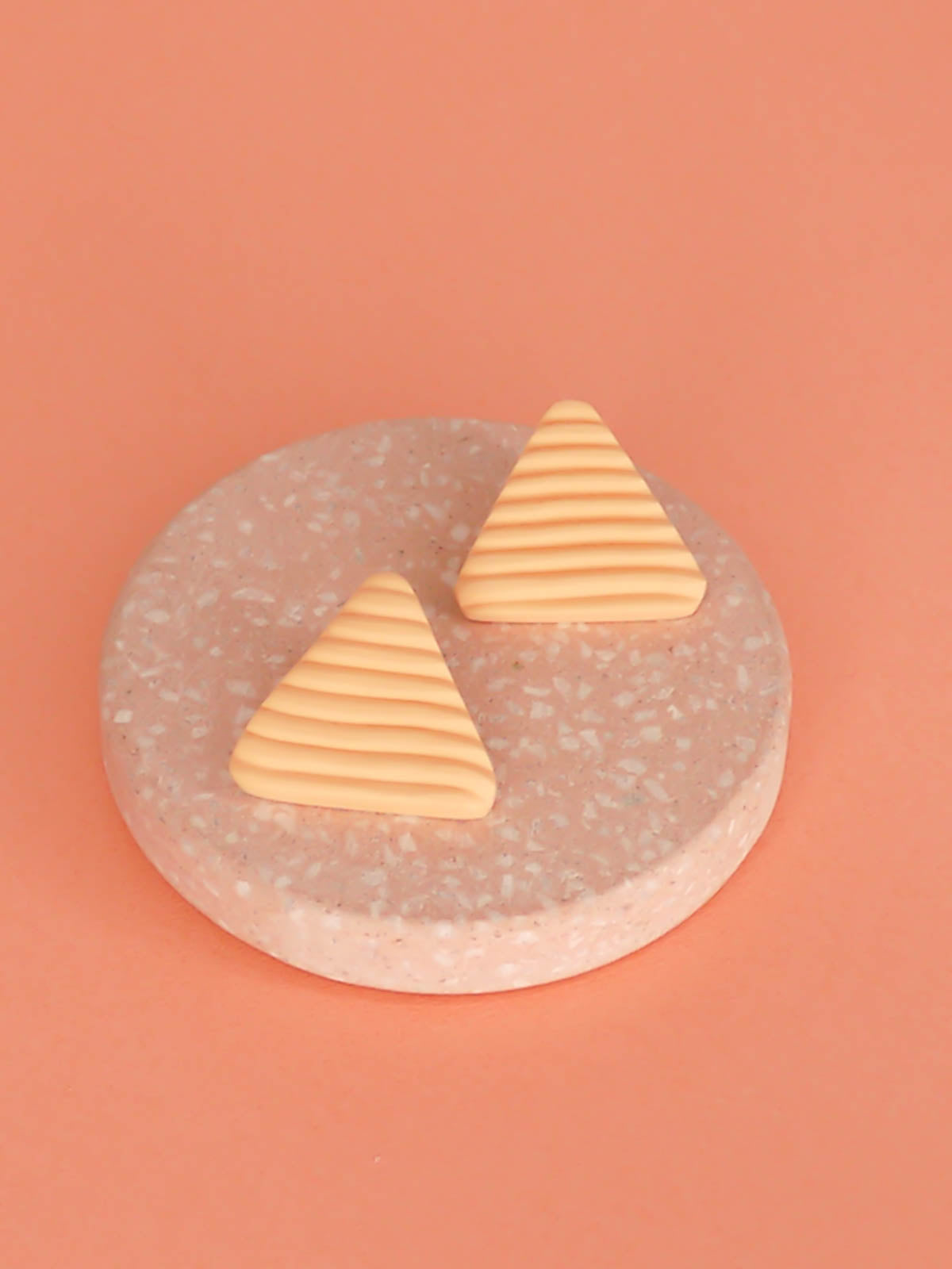 Lightweight peach polymer clay triangle stud earrings in a fluted striped texture with stainless steel studs.