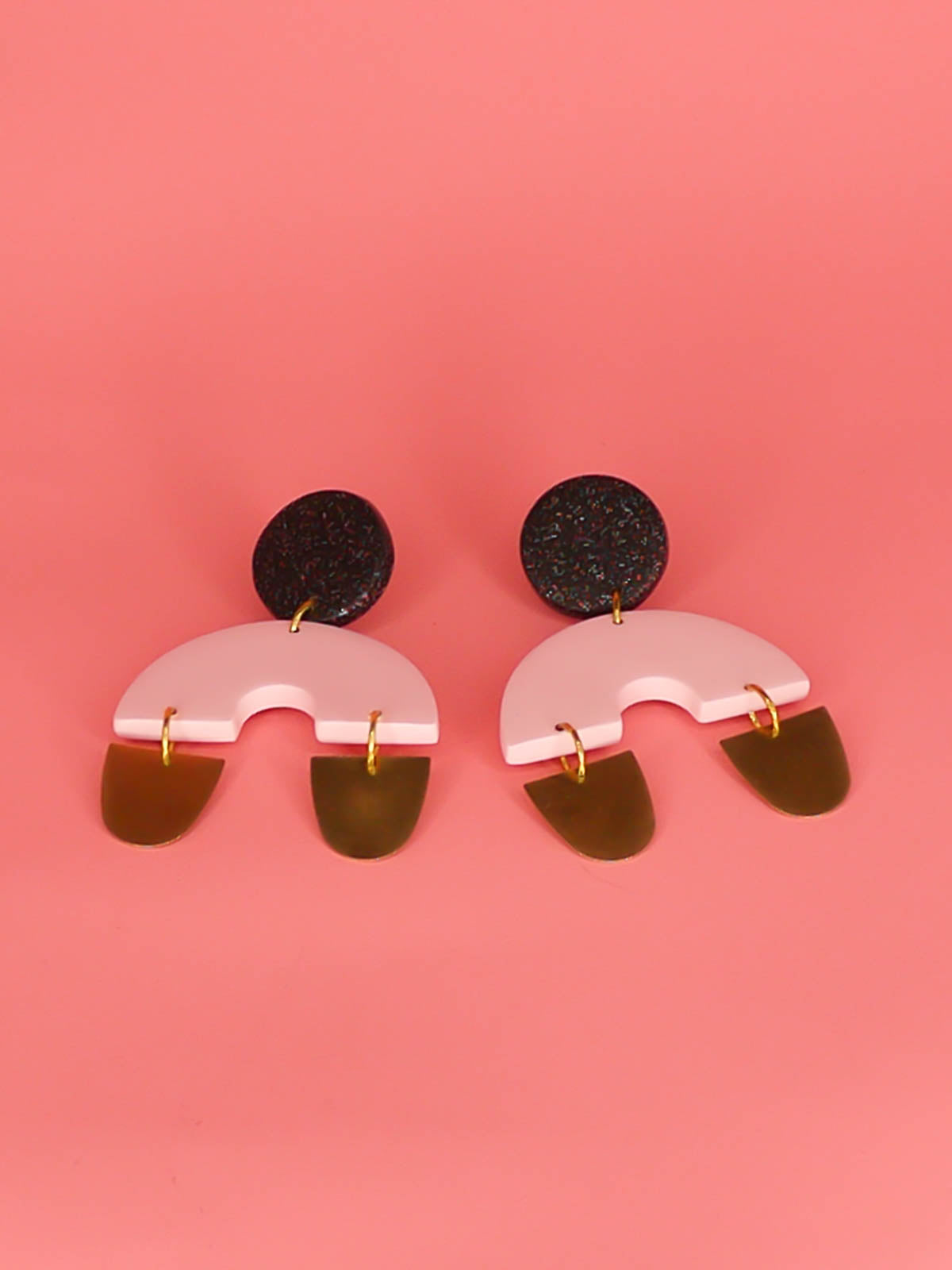 Large geometric arch dangle chandelier earrings with a black glitter stud, connected to a pink semi circle with two brass semi circles hanging off either side of the arch. Made from polymer clay with stainless steel posts.