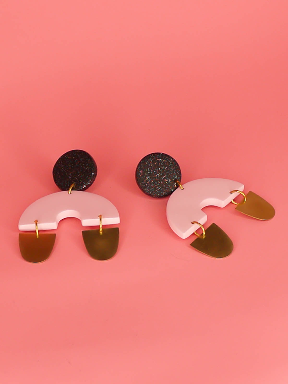 Large geometric arch dangle chandelier earrings with a black glitter stud, connected to a pink semi circle with two brass semi circles hanging off either side of the arch. Made from polymer clay with stainless steel posts.