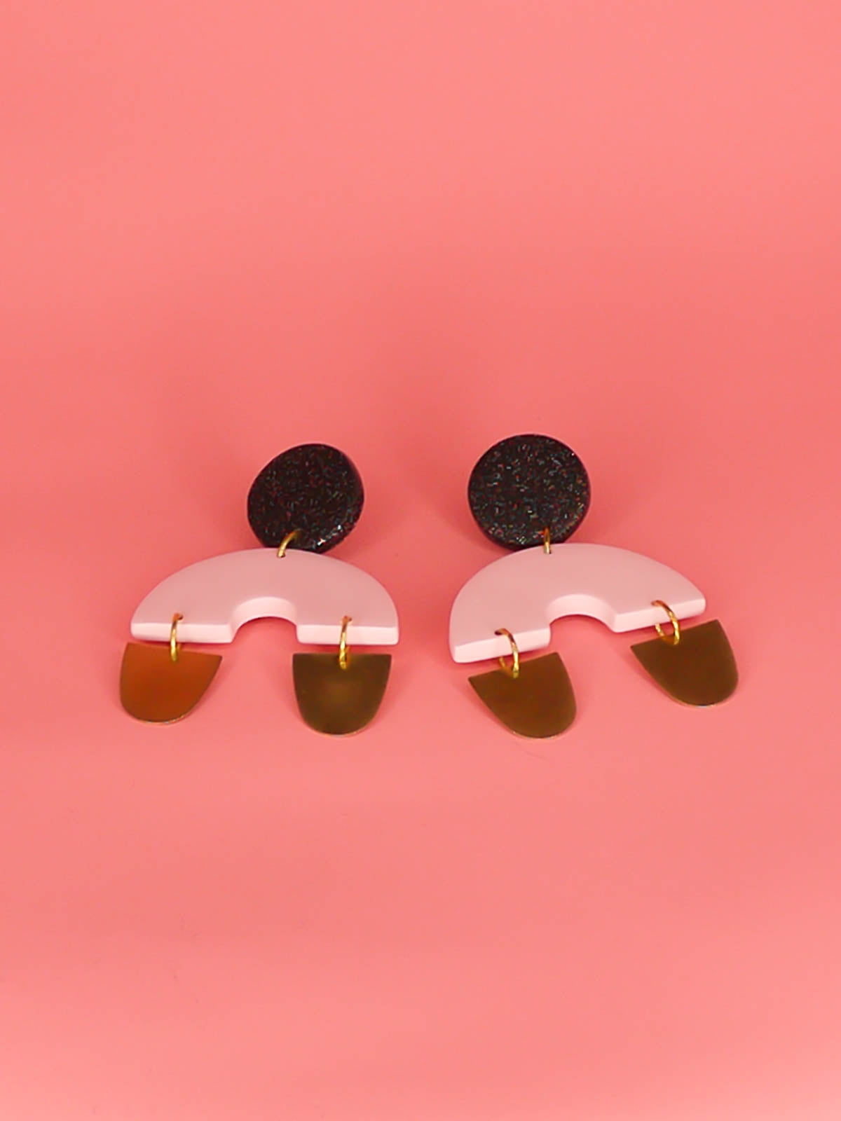 Large geometric arch dangle chandelier earrings with a black glitter stud, connected to a pink semi circle with two brass semi circles hanging off either side of the arch. Made from polymer clay with stainless steel posts.