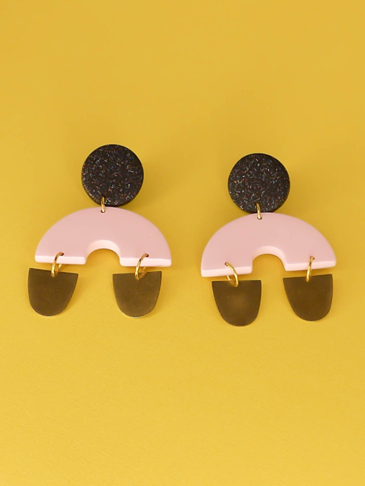 Large geometric arch dangle chandelier earrings with a black glitter stud, connected to a pink semi circle with two brass semi circles hanging off either side of the arch. Made from polymer clay with stainless steel posts.