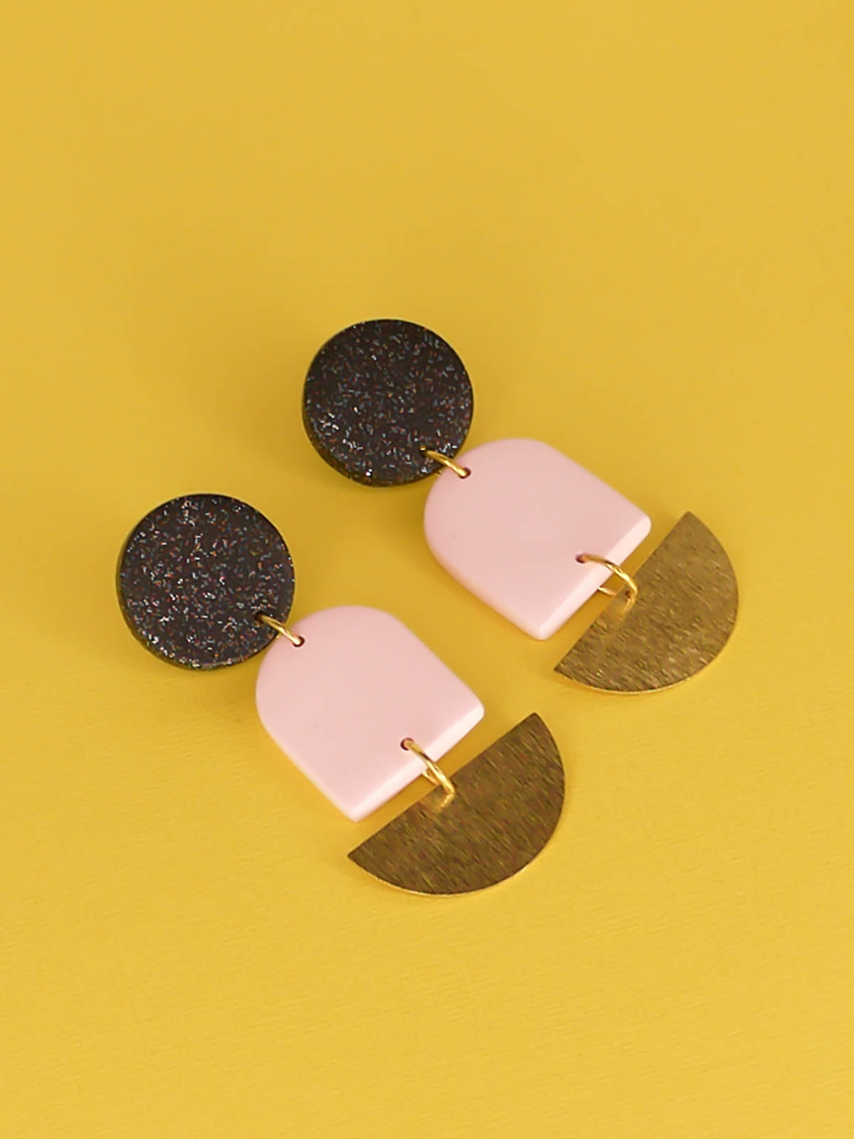 Geometric lightweight arch statement earrings with a black glitter polymer clay stud, a pale pink polymer arch and a textured brass semi circle