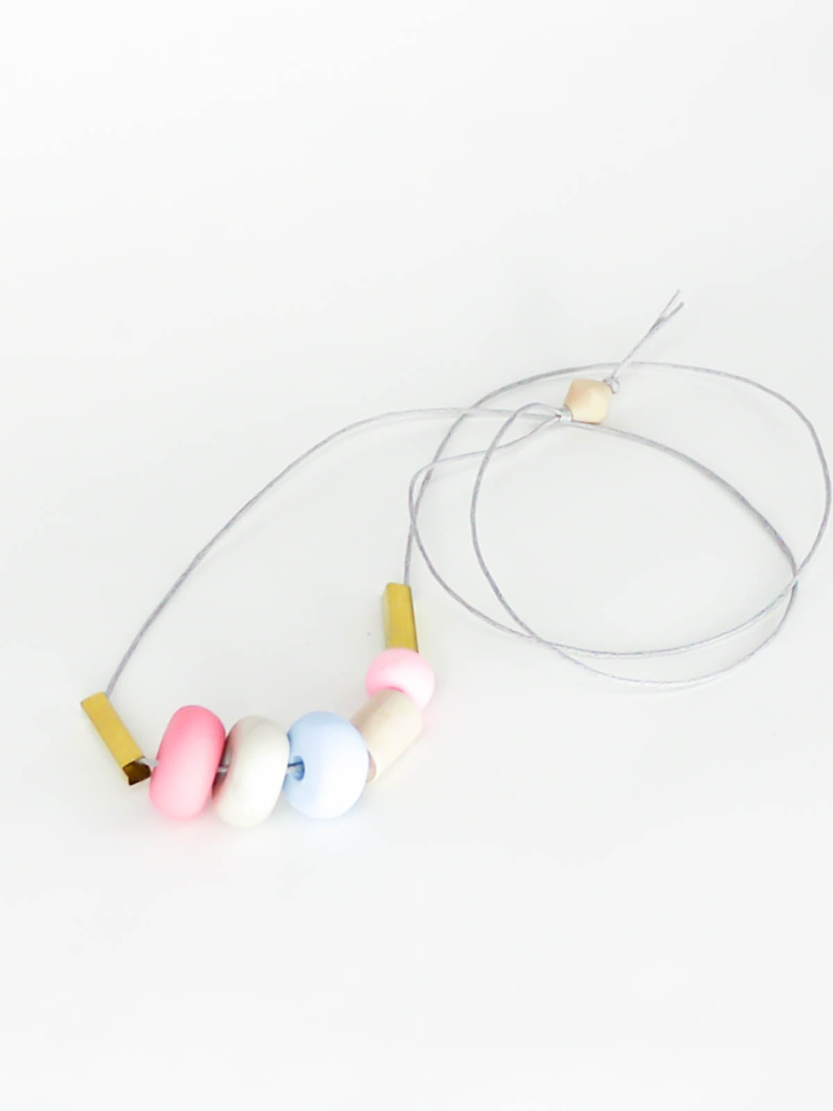 Lightweight geometric colourful bead necklace with 3 handmade polymer clay beads in pink, marble & blue- wood tube bead & pink wood bead, brass tube beads on either side, strung on a cotton cord with a wood bead knotted at the end