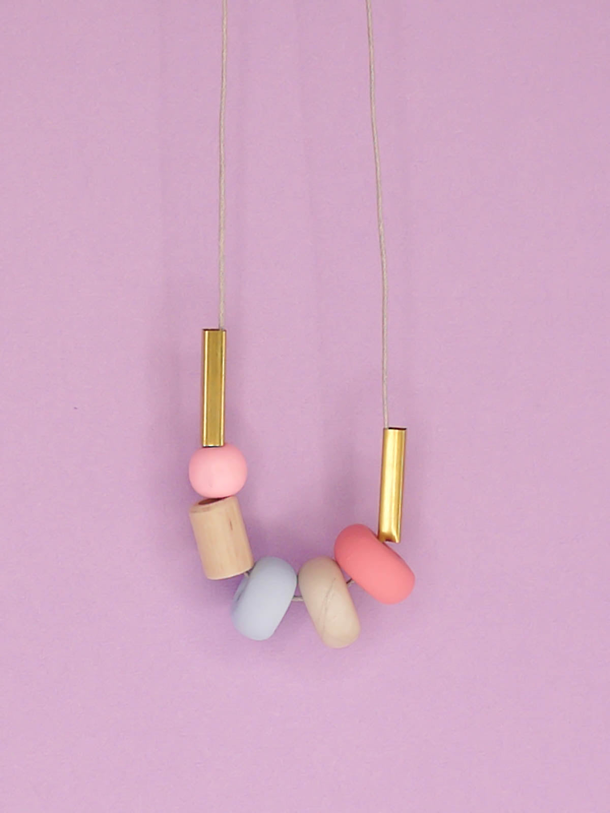 Lightweight geometric colourful bead necklace with 3 handmade polymer clay beads in pink, marble & blue- wood tube bead & pink wood bead, brass tube beads on either side, strung on a cotton cord with a wood bead knotted at the end