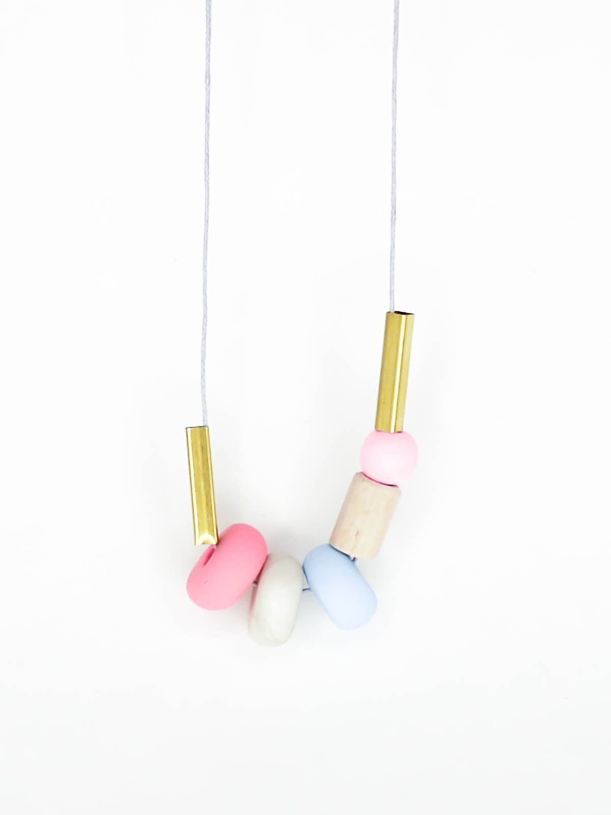 Lightweight geometric colourful bead necklace with 3 handmade polymer clay beads in pink, marble & blue- wood tube bead & pink wood bead, brass tube beads on either side, strung on a cotton cord with a wood bead knotted at the end