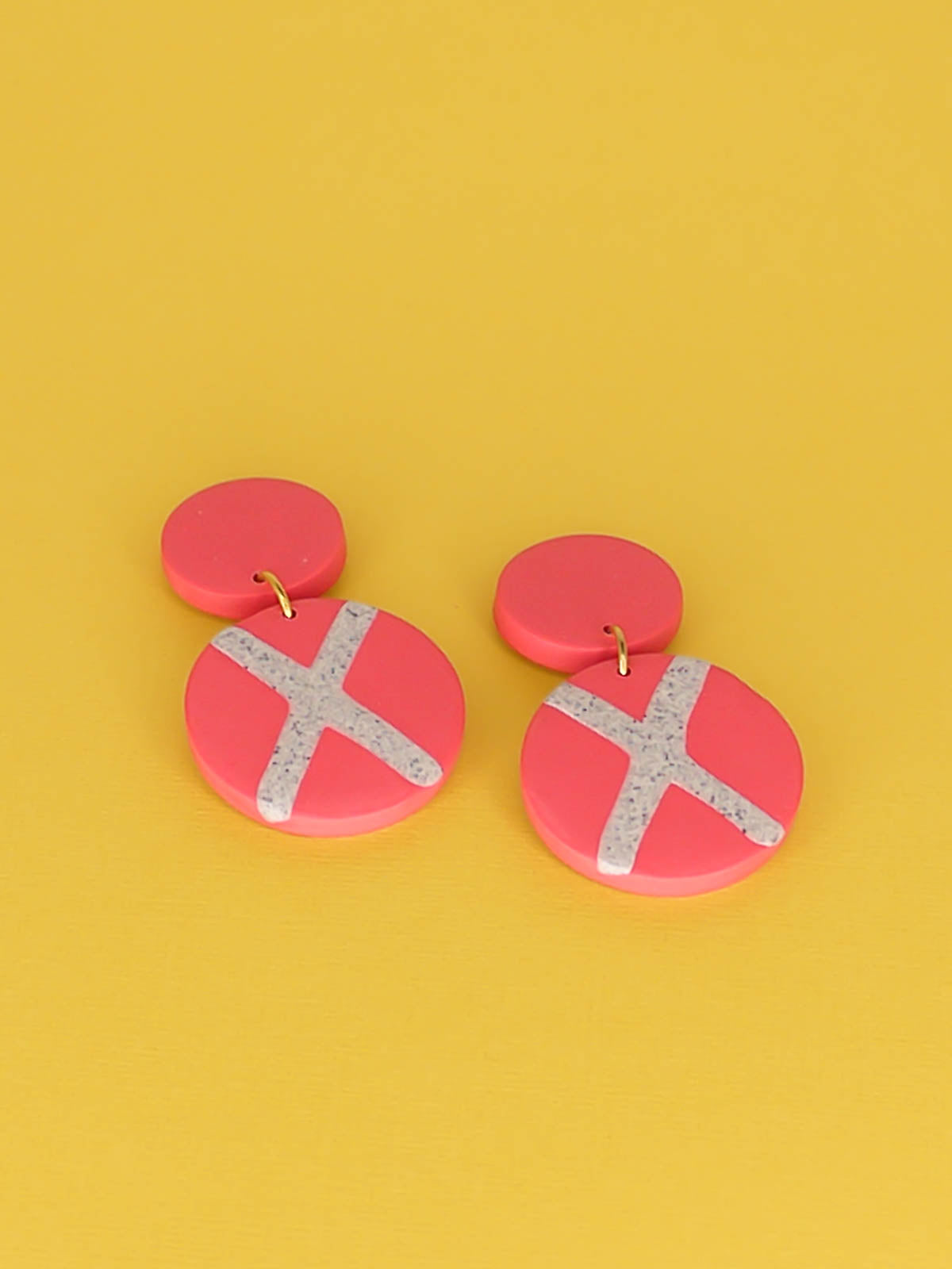 Polymer clay dangle statement earrings with a pink stud connected to a pink circle with a granite cross in the centre