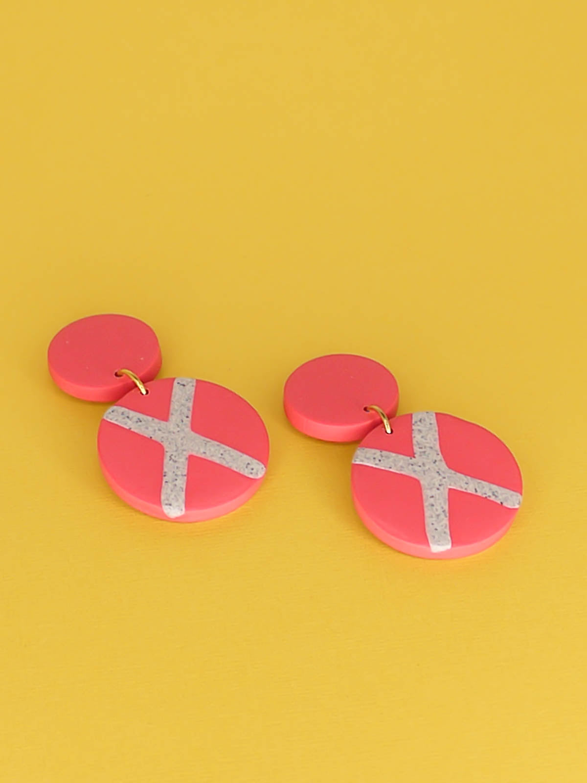 Polymer clay dangle statement earrings with a pink stud connected to a pink circle with a granite cross in the centre